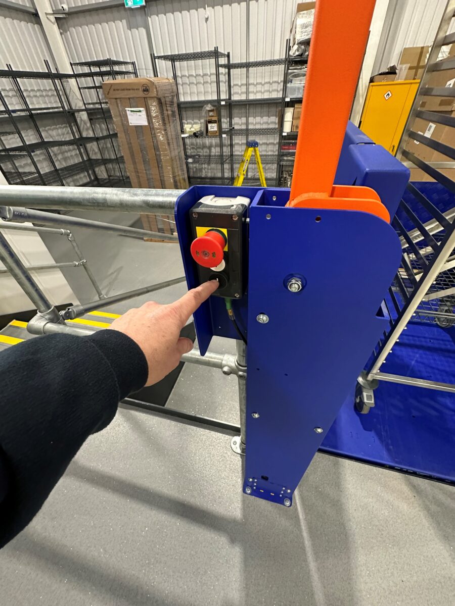 A finger pointing at a red emergency stop button attached to a MCL low rise lift.
